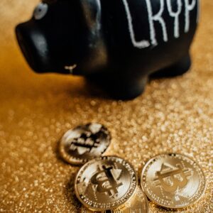 A black piggy bank labeled 'Crypto' with golden bitcoin coins on a sparkling gold surface.